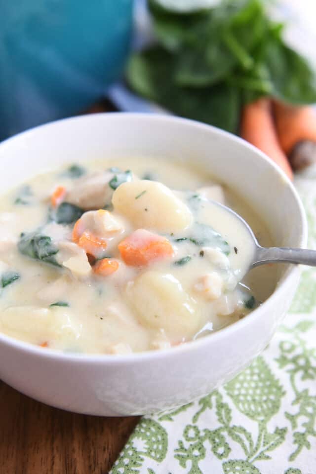 Spoon scooping out bite of creamy chicken gnocchi soup in white bowl.