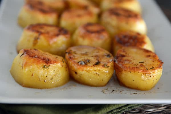 Golden brown roasted potatoes on a white platter.