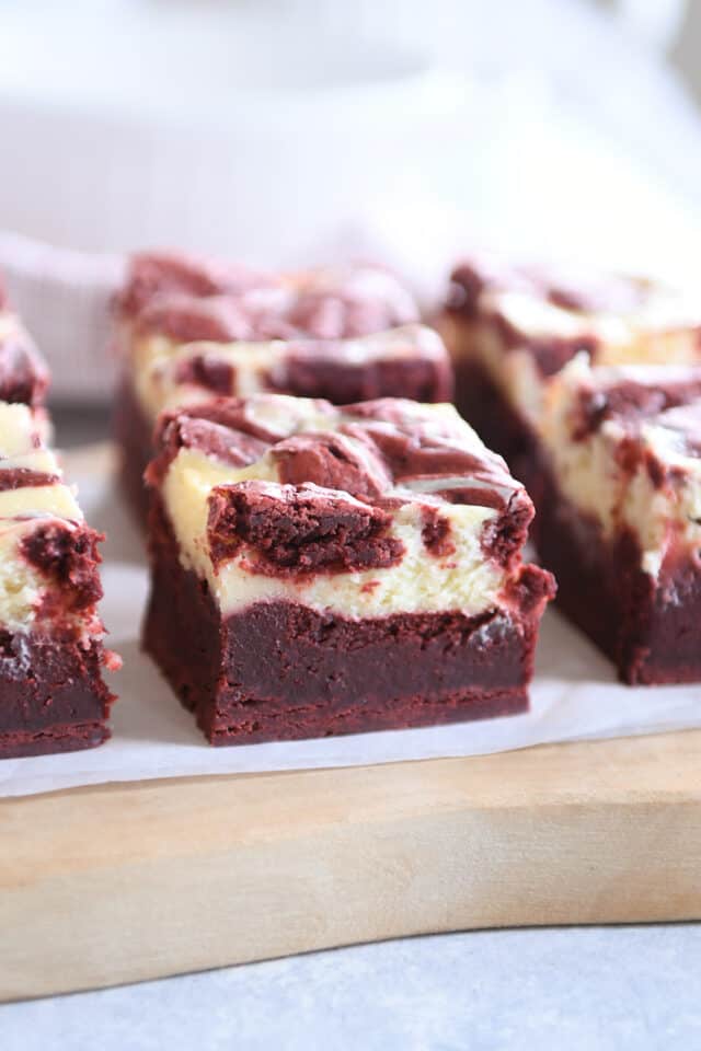 Red velvet cheesecake brownie on wood cutting board.