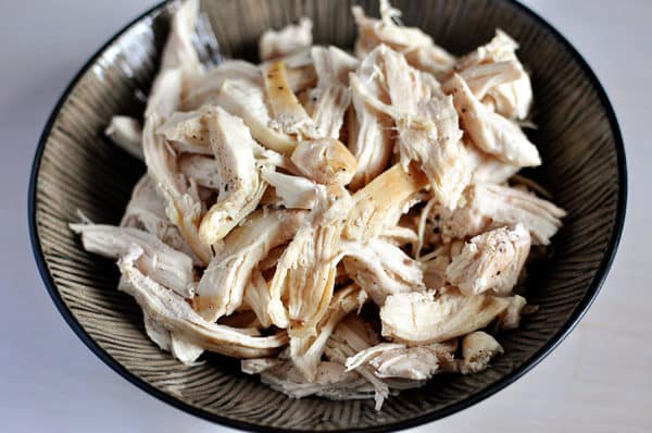 Cooked shredded, salted and peppered chicken, in a large ceramic bowl.