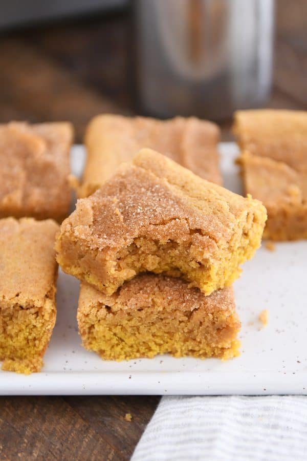 Two pumpkin snickerdoodle bars stacked on white tray with bite taken out of top bar.