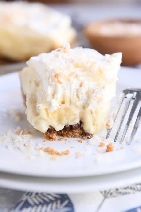 Bite taken out of banana coconut cream pie on white plate with fork.
