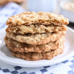 Four crispy oatmeal cookies stacked on white plate.