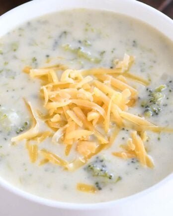 Broccoli cheese soup in white bowl with cheddar cheese.