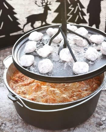 Lifting lid from Dutch oven with coals on top.