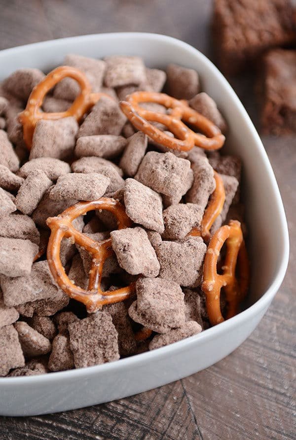 A white bowl full of chocolate muddy buddies and pretzels.