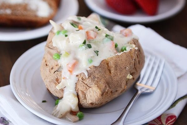 A baked potato split open and topped with chicken pot pie sauce.