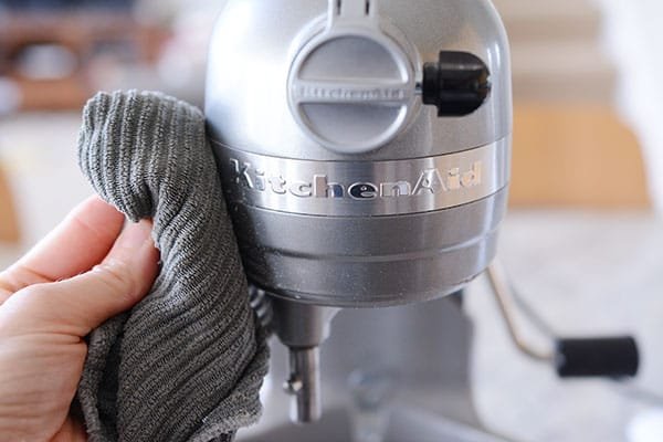 A kitchen rag wiping off a silver KitchenAid mixing bowl.