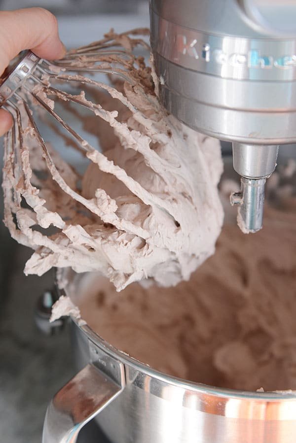 Whipped chocolate frosting on a KitchenAid whisk above the bowl.