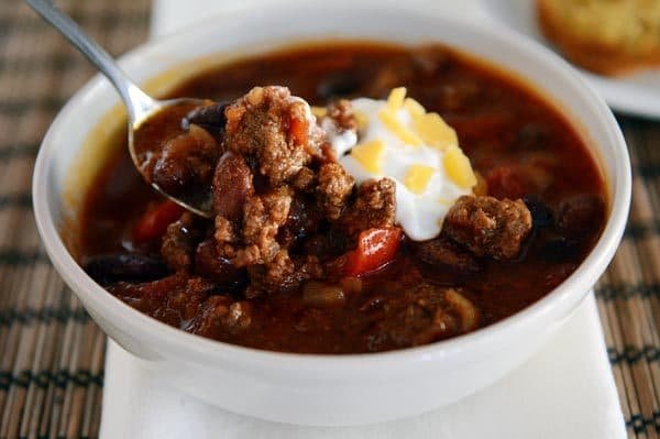 A white bowl of beef chili with sour cream and cheese on top.