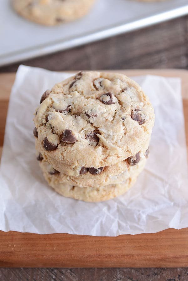 Three chocolate chip cookies stacked on top of each other on a piece of parchment.