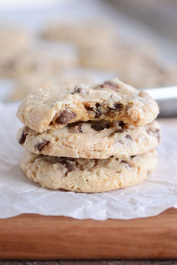Three chocolate chip cookies stacked on each with a bite taken out of the top cookie.